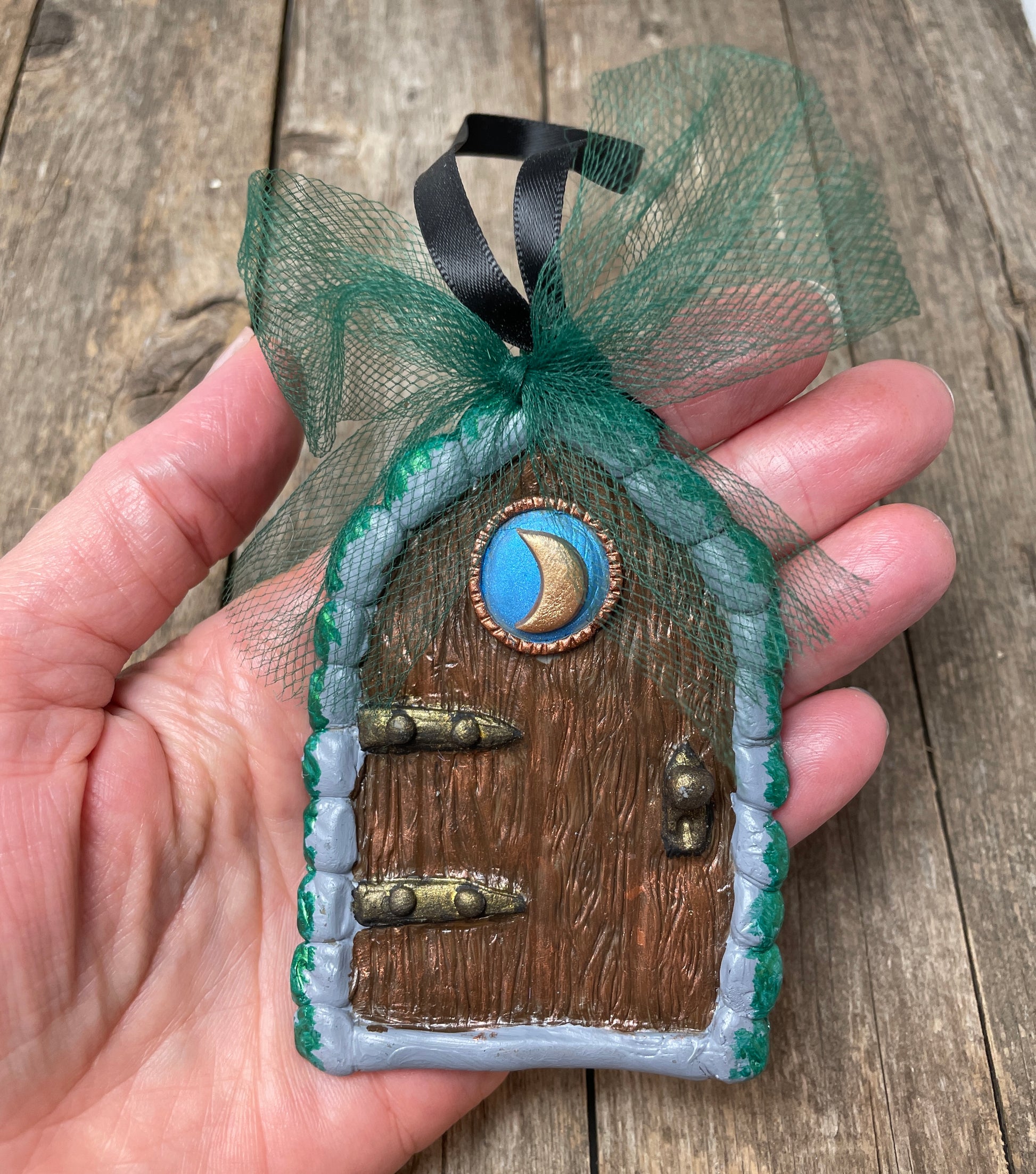 Moon fairy door ornament with green tulle  bow  held in a hand.