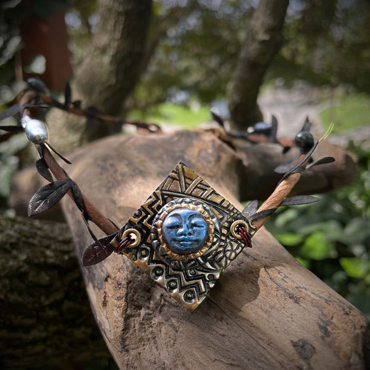 Blue moon on a golden textured diamond shape focal  on a brown wire leaf crown resting on a tree branch.