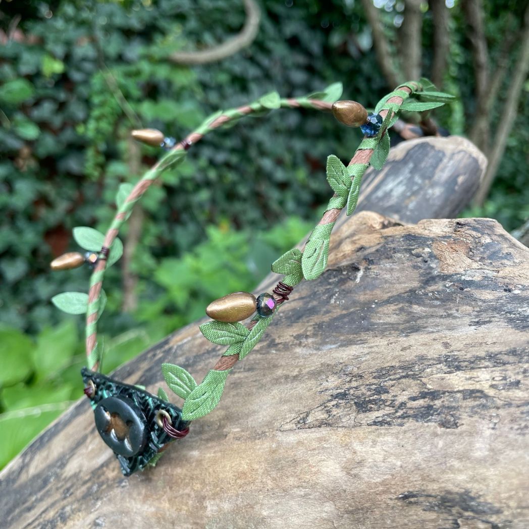 Silver and green triple moon focal on a brown wire and green leaf crown resting on a branch.