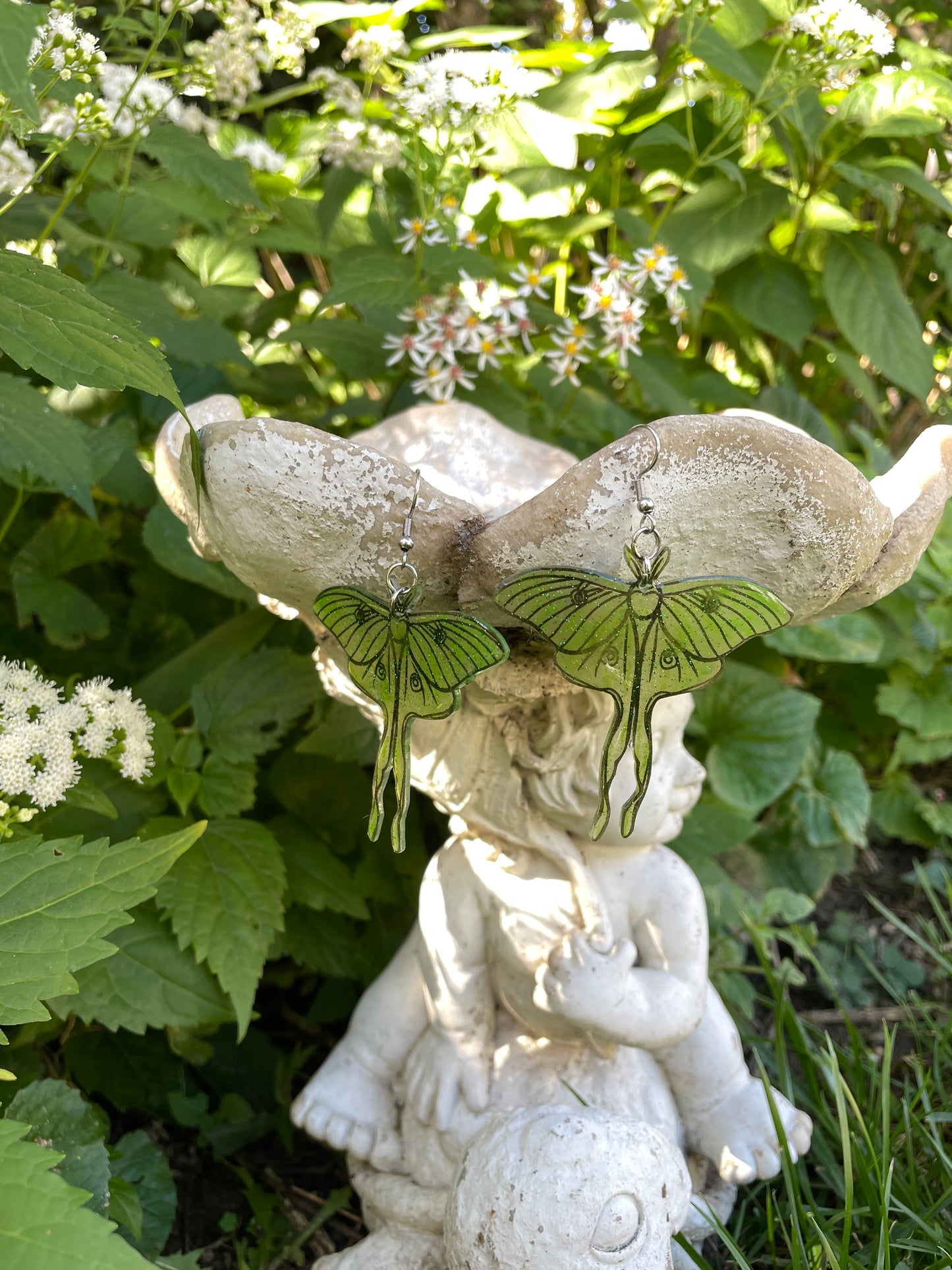 Green luna moth earrings hanging on a garden ornament.