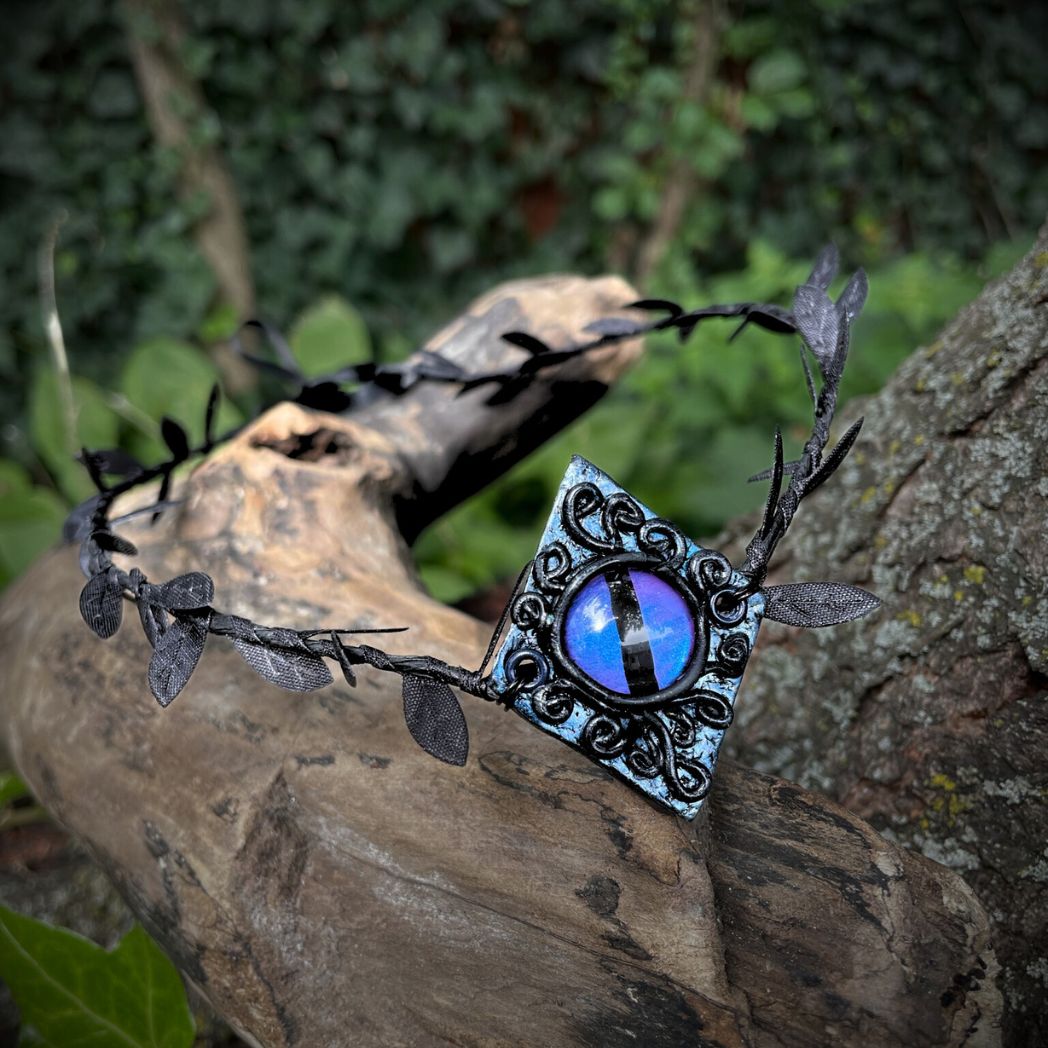 Purple dragon on a diamond shape textured clay base on a black leaf wire headband resting on a tree branch.