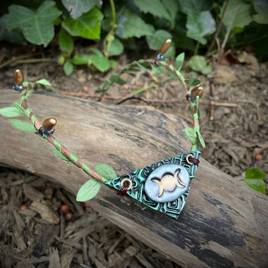 Silver and green triple moon focal on a brown wire and green leaf  crown resting on a branch.