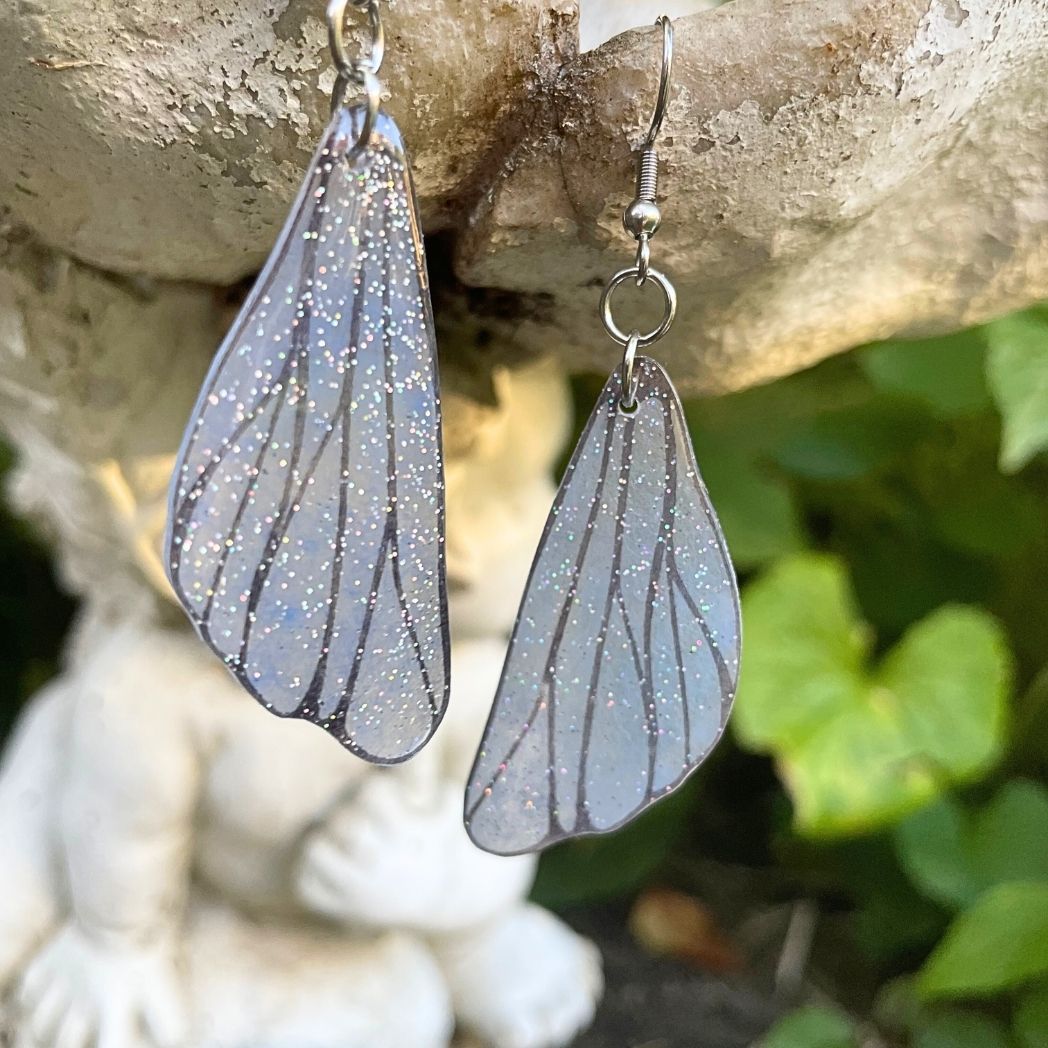 gray small wing earrings hanging on a garden ornment.