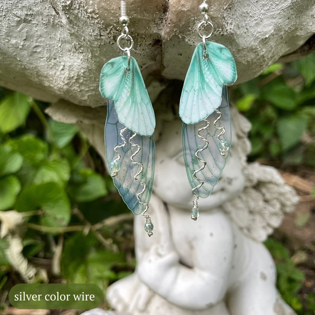 Mint green double wing fairy wings with silver twisted wires with crystals and silver french ear hooks hanging on a angel garden ornament.