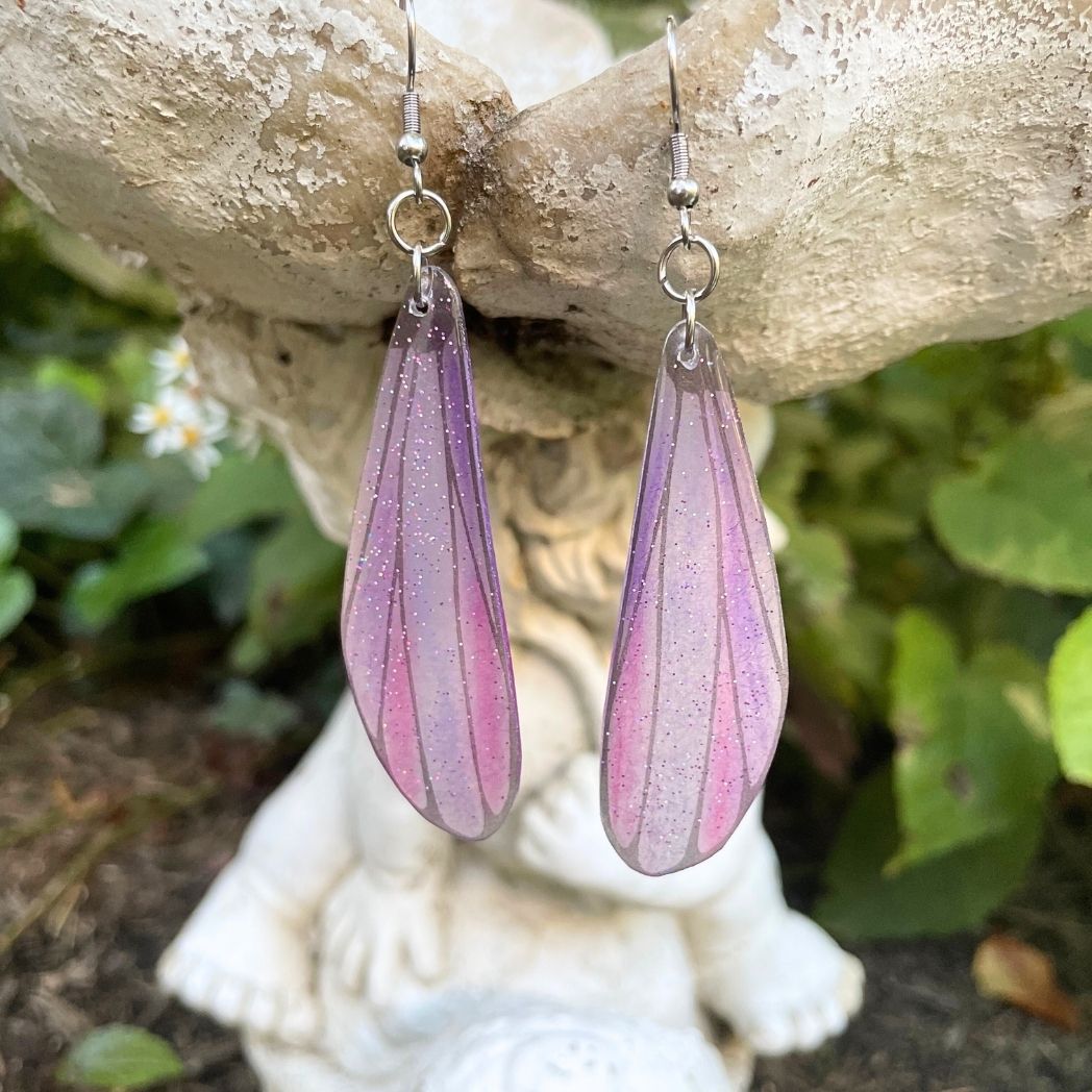Pink sparkly long dangle dragonfly earrings dangling from a garden ornment.