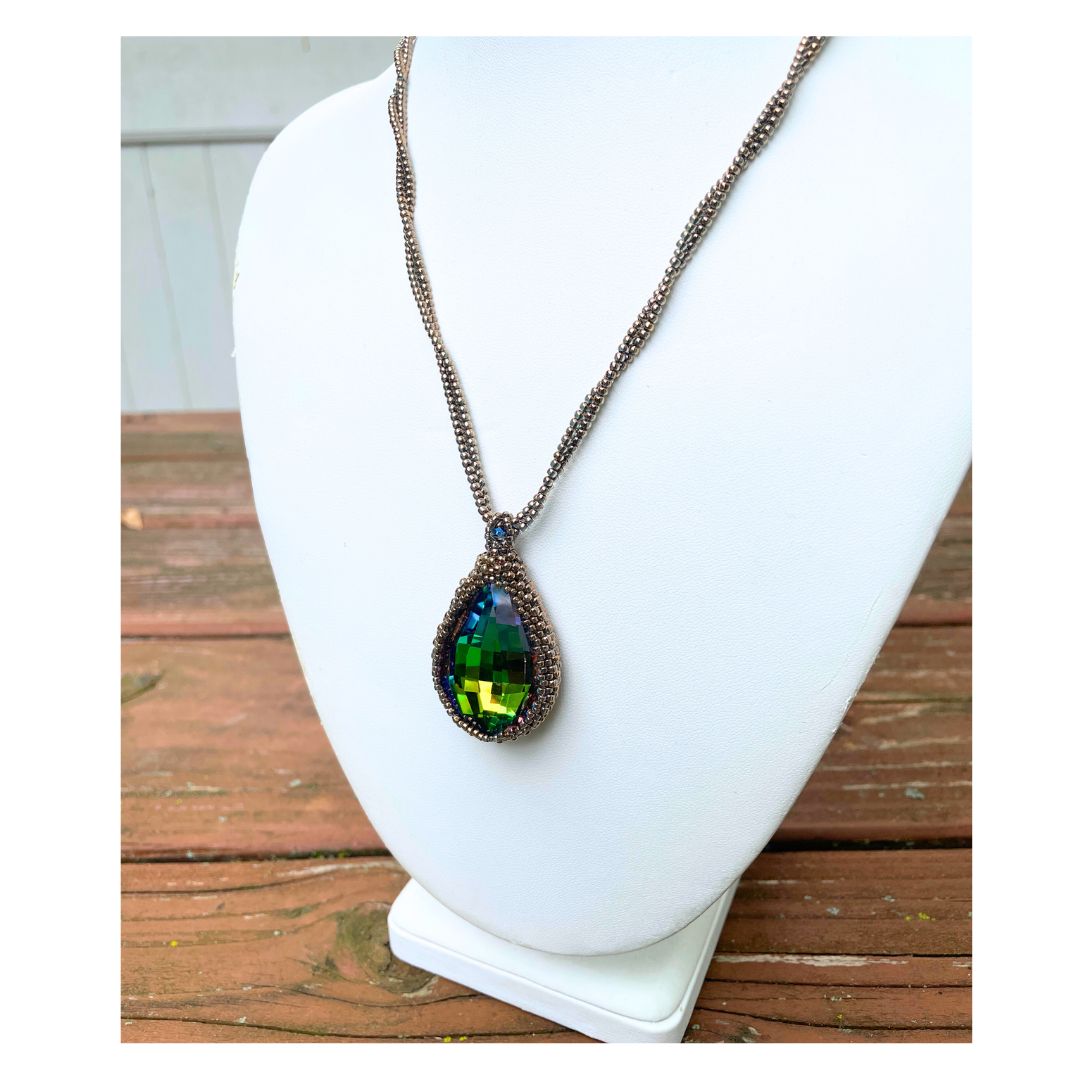 large beaded teardrop shaped rainbow crystal necklace with twisted beaded chain with an iridescent button closure on a display bust.