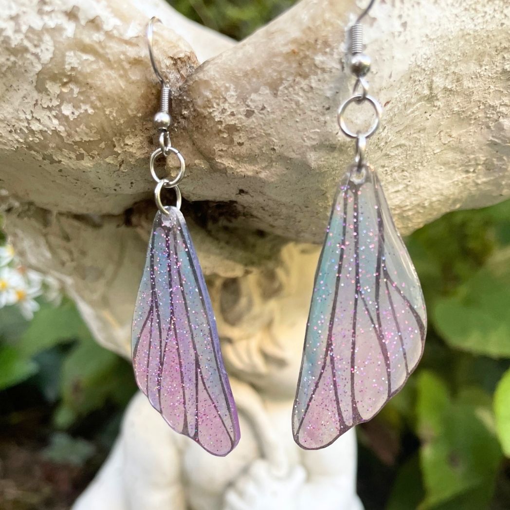 pink and blue wing earrings hanging from a garden ornament.