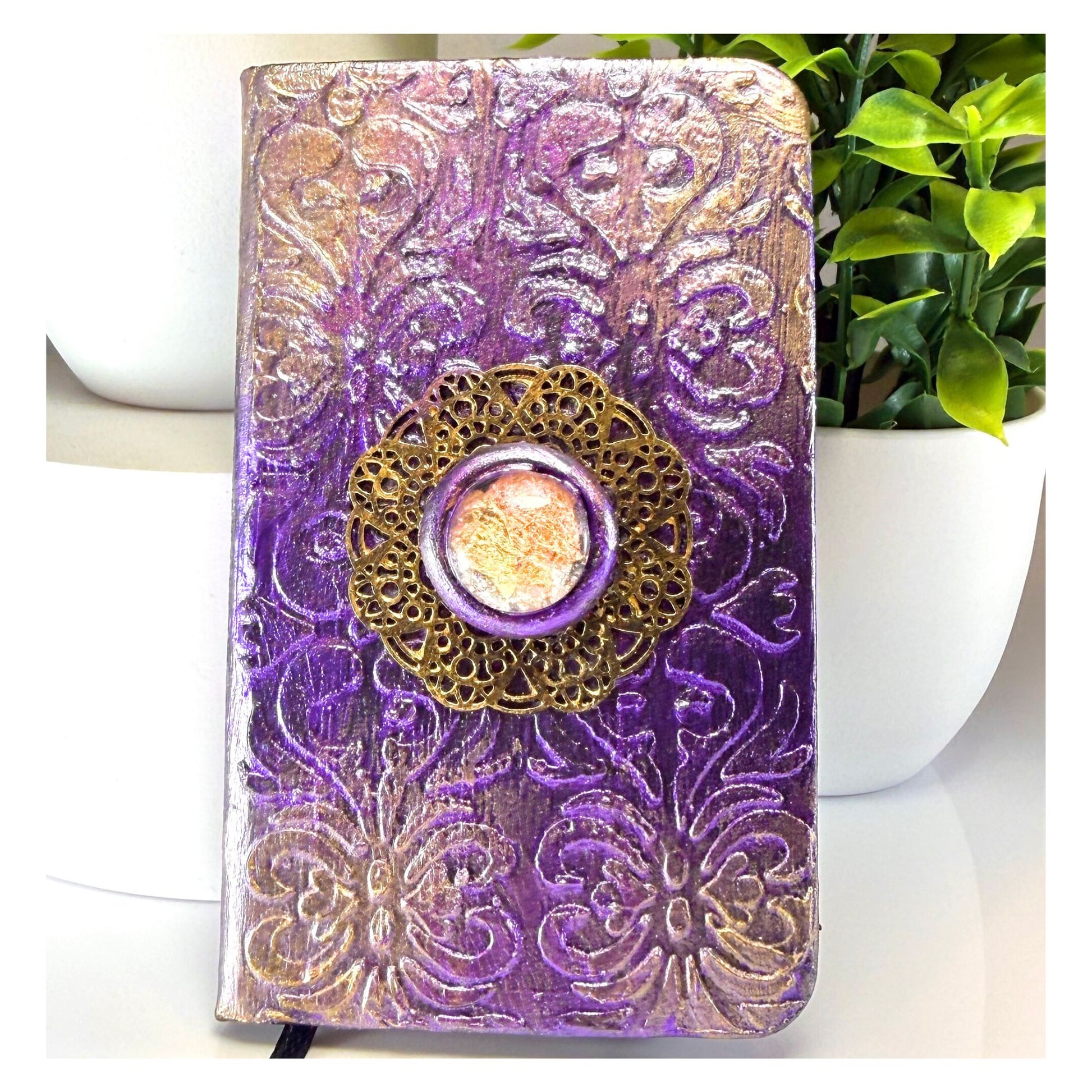 Decorative purple and gold notebook with a central embellishment on a white surface.