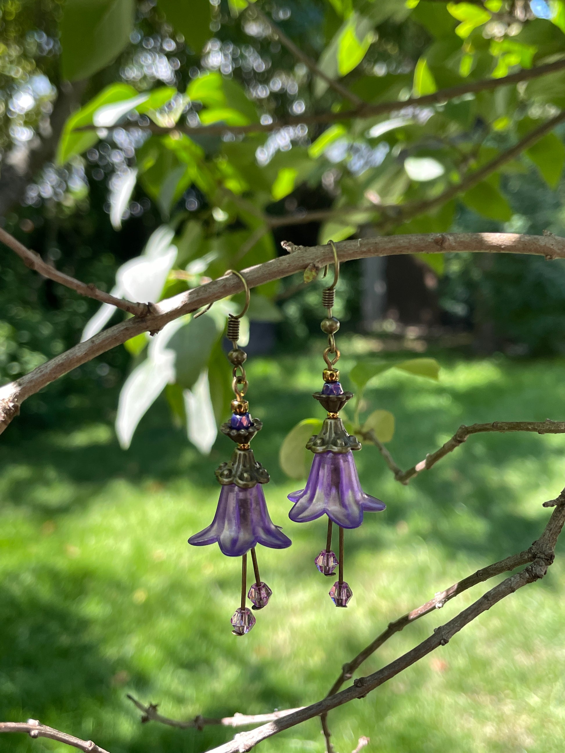 purple bell flower dangle earrings with clear crystal stamen and antique bronze accent beads on a white model bust in a garden setting.