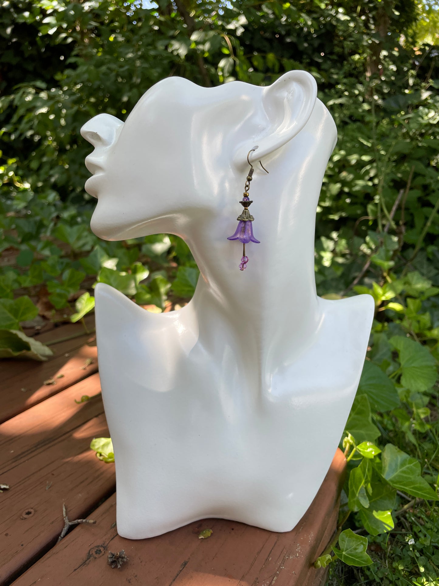 purple bell flower dangle earrings with clear crystal stamen and antique bronze accent beads on a white model bust in a garden setting.