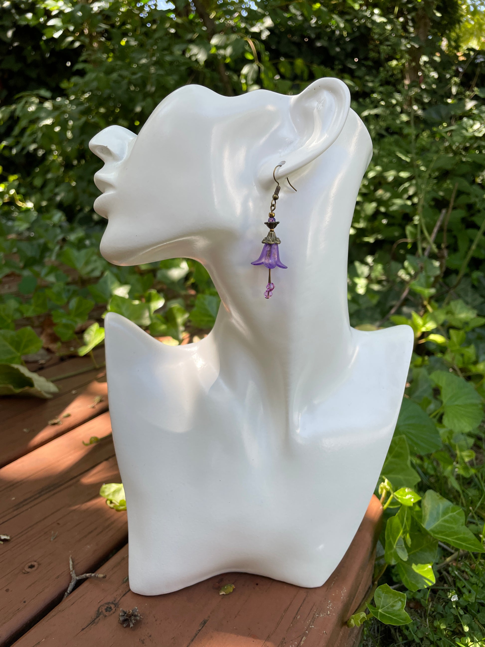 purple bell flower dangle earrings with clear crystal stamen and antique bronze accent beads on a white model bust in a garden setting.