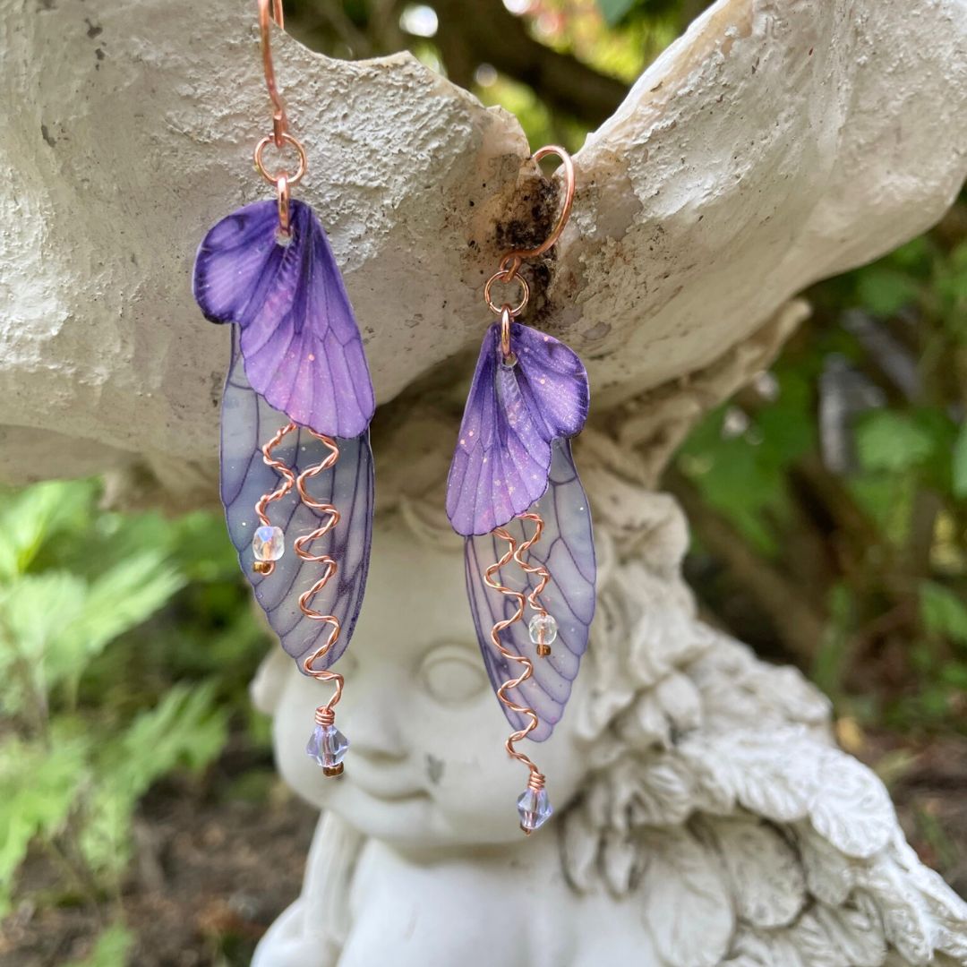purple butterfly wing earrings with lavender crystals and copper wires. Hanging from fairy garden ornament.