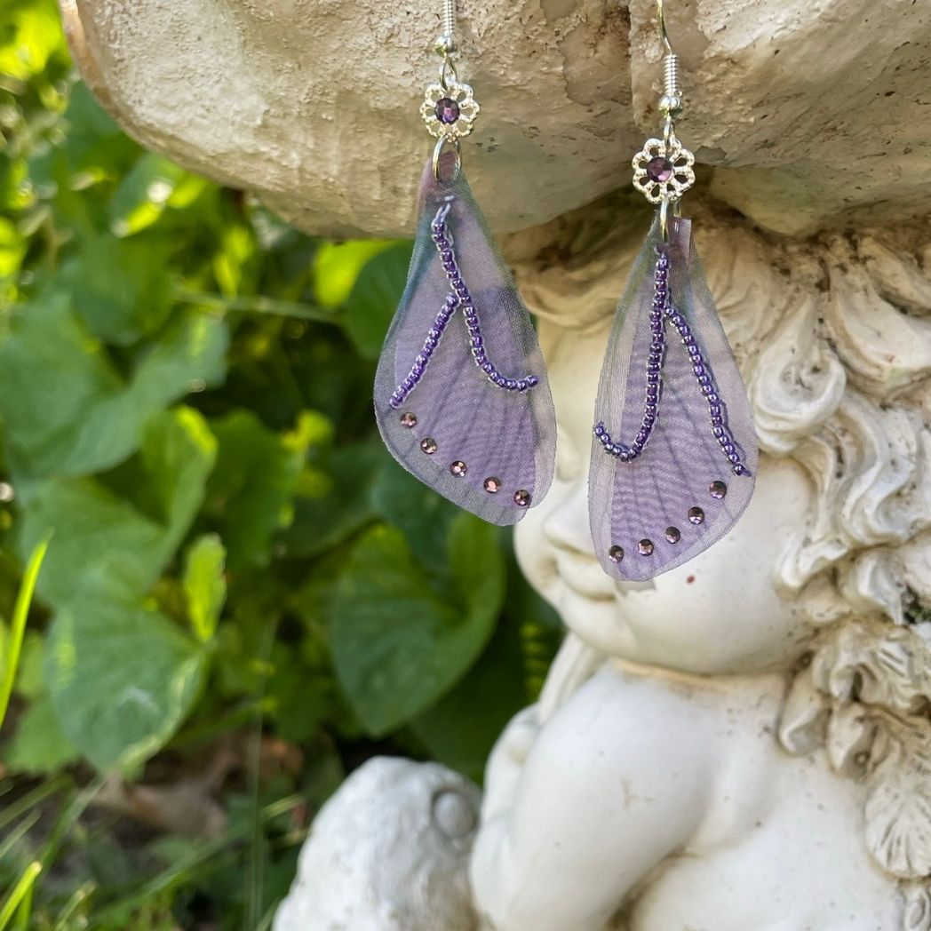 purple beaded fabric wing earrings with purple crystals and a flower bead with purple crystal above  wings connecting to the ear wires