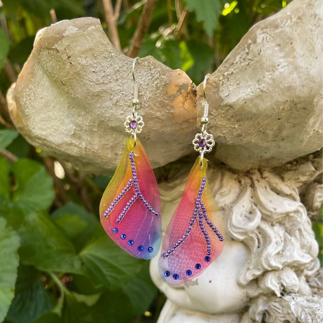 Colorful rainbow sheer fabric with beading and blue crystals. A flower bead with a crystal connects the wings to the ear wires.