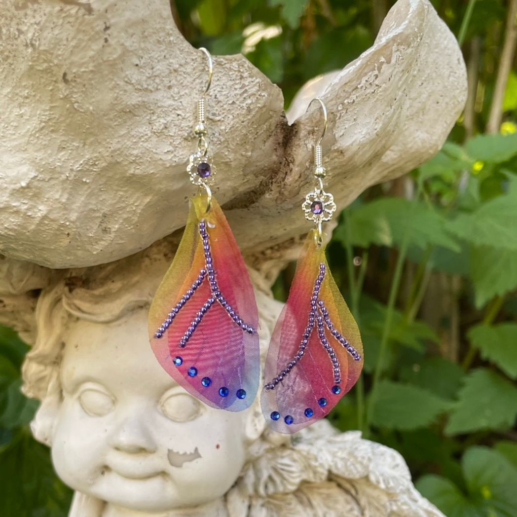 Colorful rainbow sheer fabric with beading and blue crystals. A flower bead with a crystal connects the wings to the ear wires.