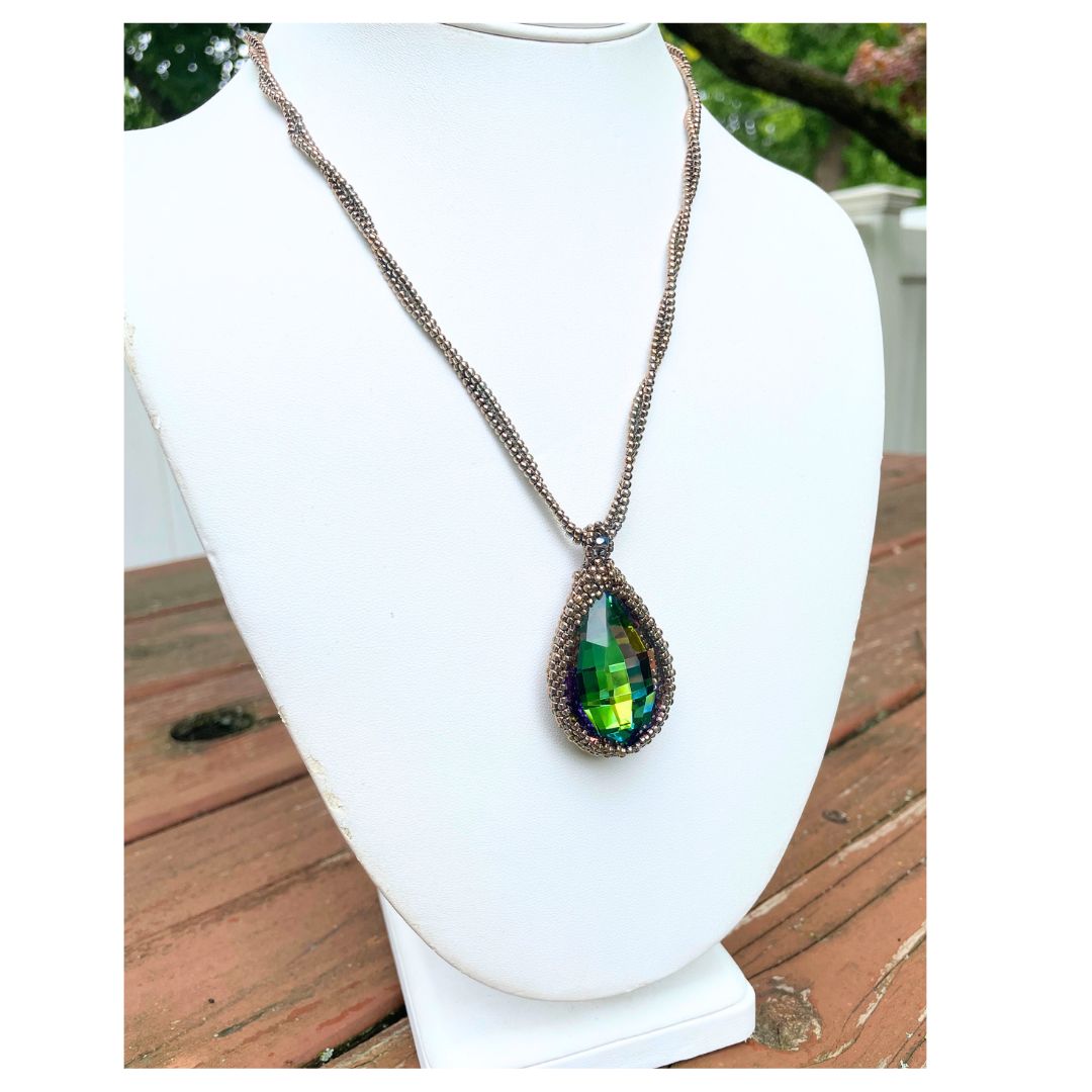 large beaded teardrop shaped rainbow crystal necklace with twisted beaded chain with an iridescent button closure on a display bust.