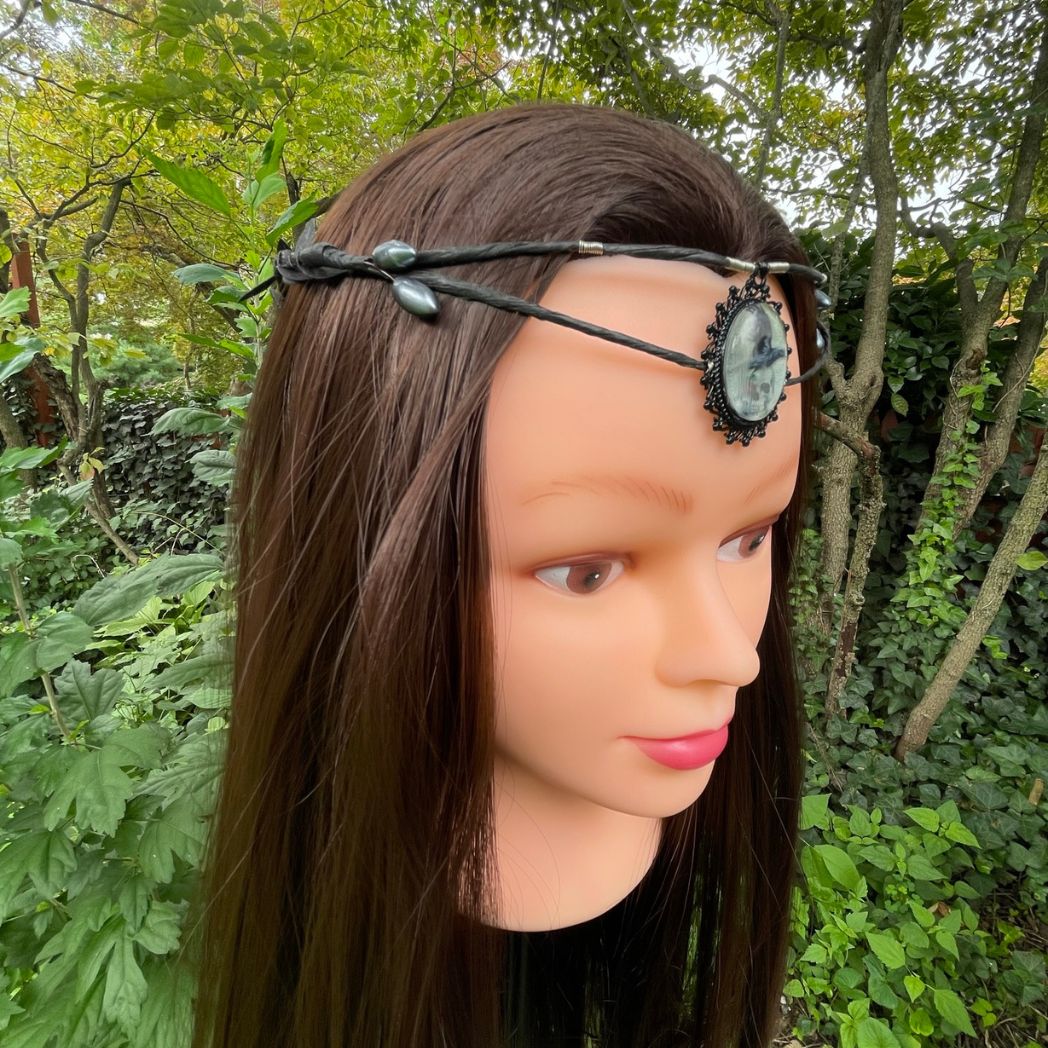 Black wire crown with oval cabochon focal of a raven and skull resting on a model.