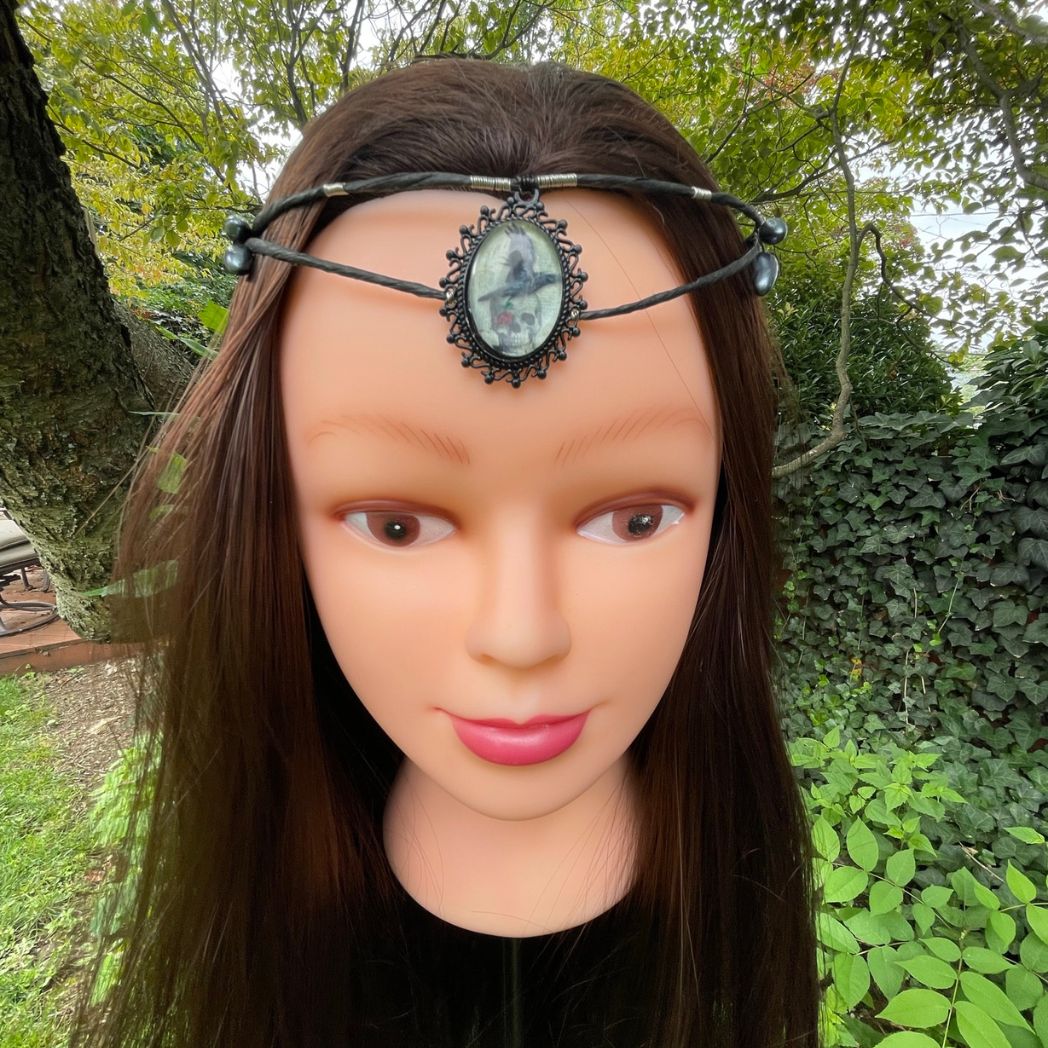 Black wire crown with oval cabochon focal of a raven and skull resting on a model.