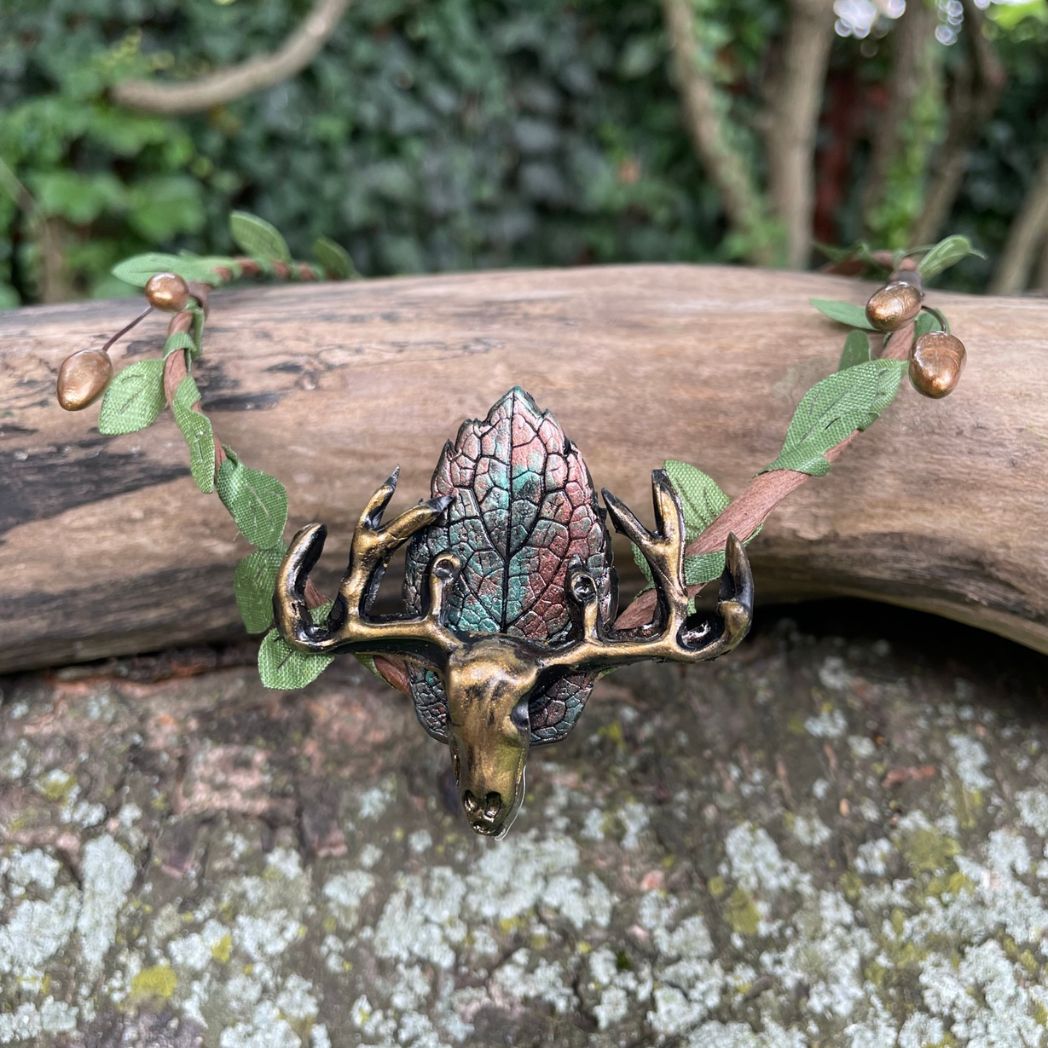 A wire crown with green leaves and a polymer clay leaf and elk focal on a tree branch.