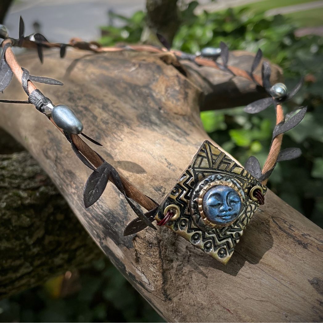 Blue moon on a golden textured diamond shape focal on a brown wire leaf crown resting on a tree branch.