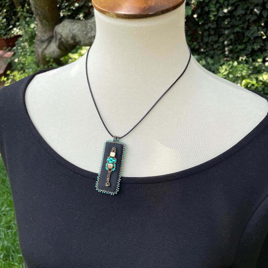 Medieval Jewelry black faux leather rectangle pendant with turquoise and gold beading with black cord necklace on mannequin