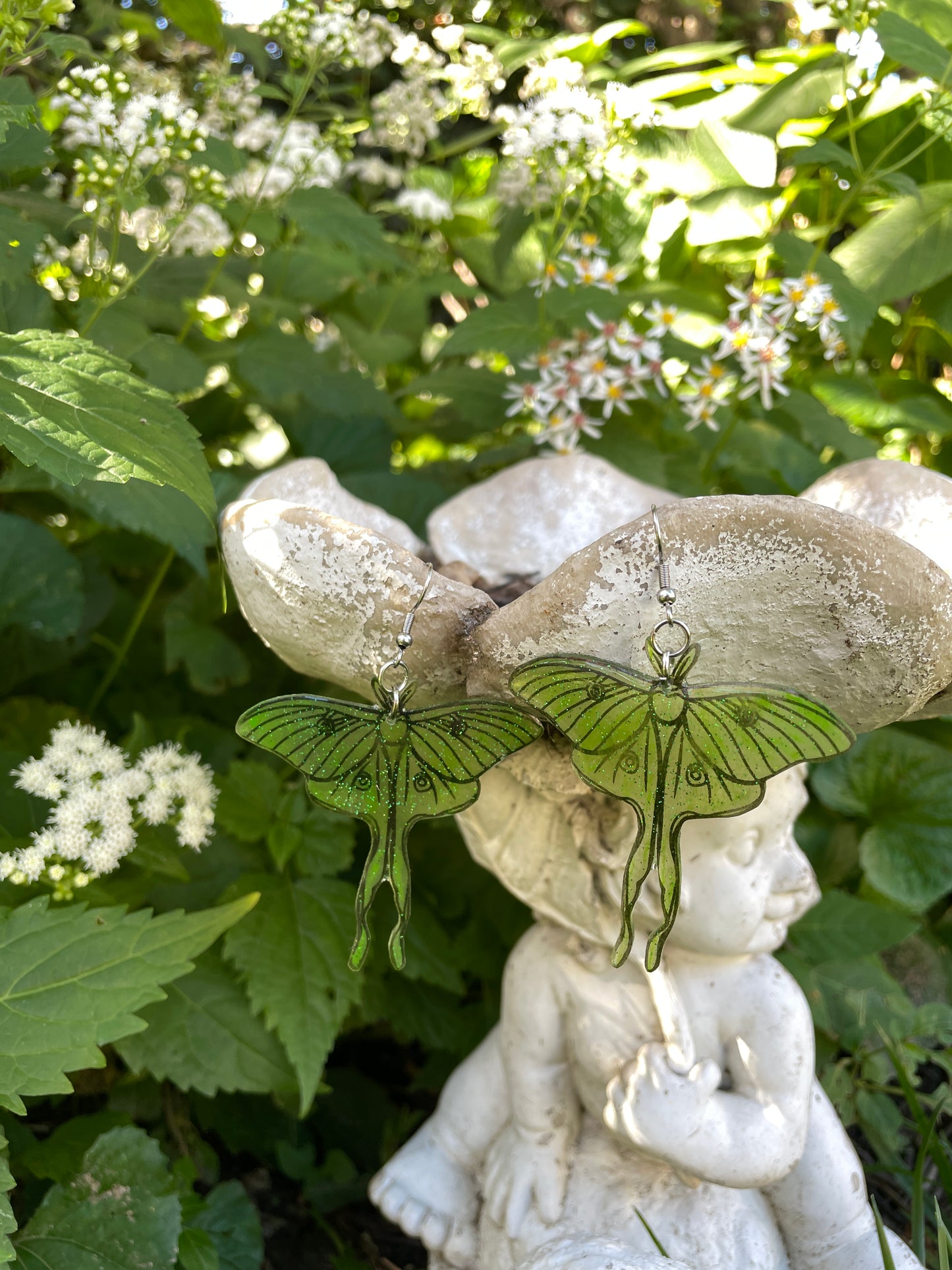 Green luna moth earrings hanging on a garden ornament.