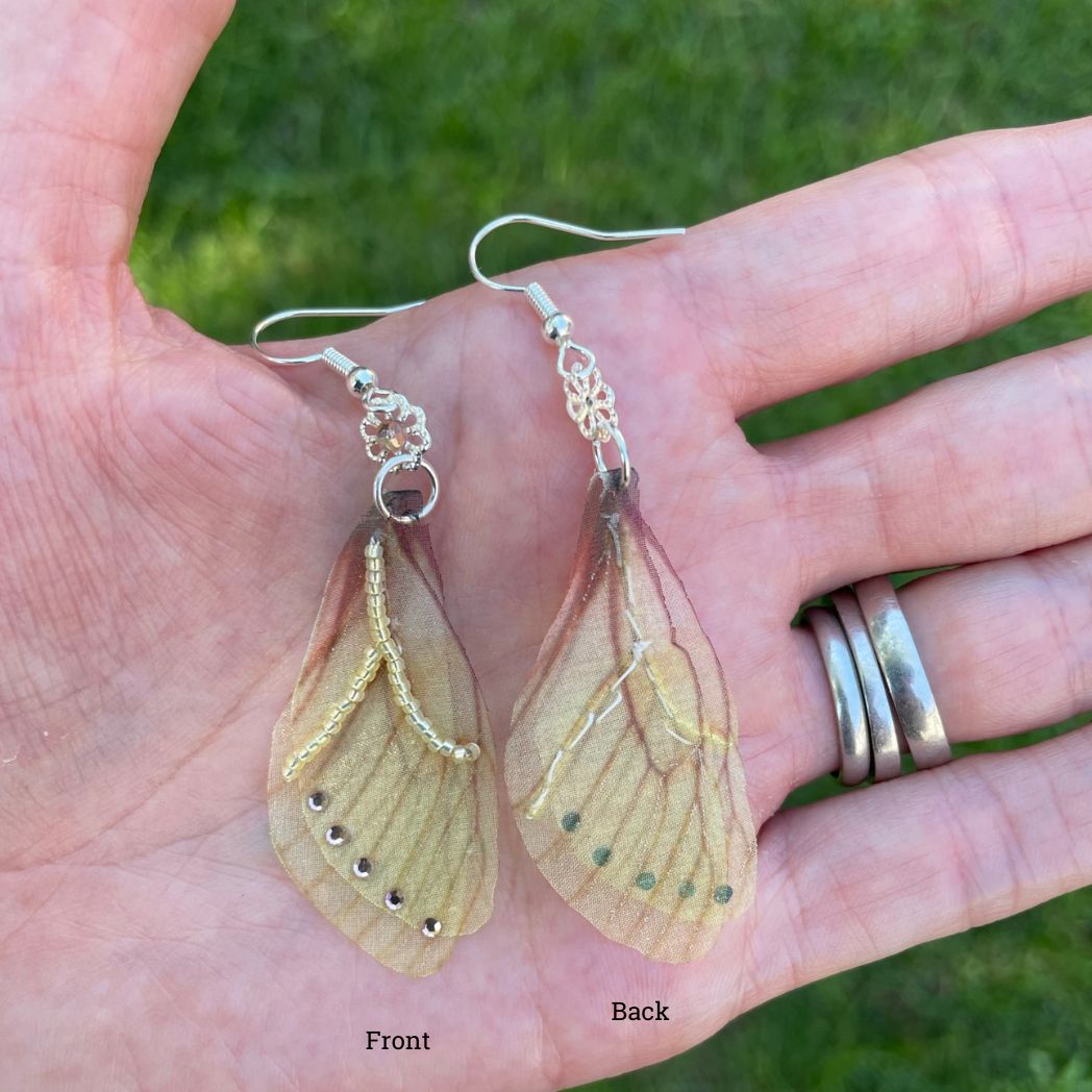 Yellow sheer fabric beaded butterfly wing earrings with peach color crystals and a flower bead connect the wings to the ear wires. Held in a hand