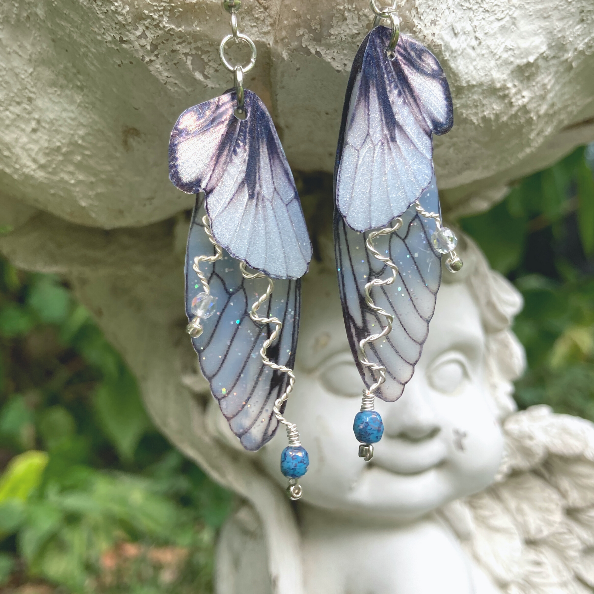 silver double wing fairy earrings with silver twisted wired branches with crystals hanging from a garden ornament