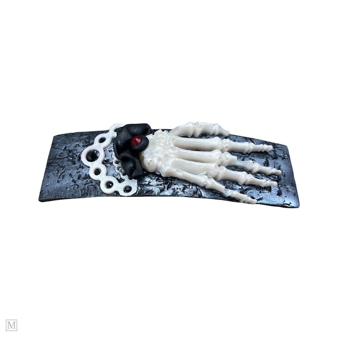 Polymer clay hair barrette with a white skeleton hand on a silver textured clip with a black and white frilly cuff.