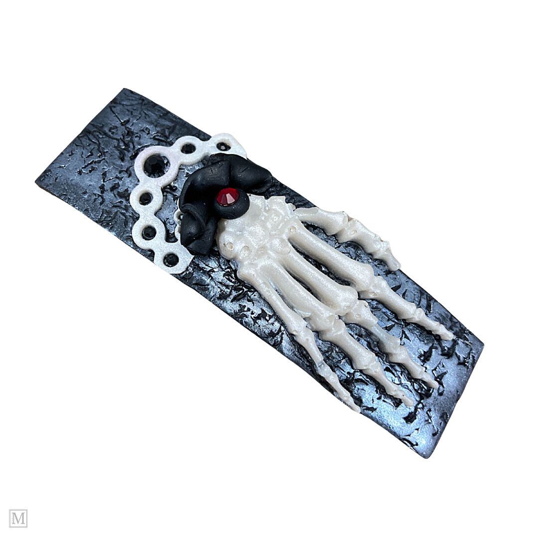 Polymer clay hair barrette with a white skeleton hand on a silver textured clip with a black and white frilly cuff.