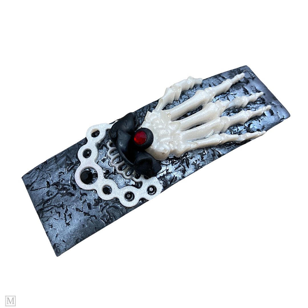 Polymer clay hair barrette with a white skeleton hand on a silver textured clip with a black and white frilly cuff.