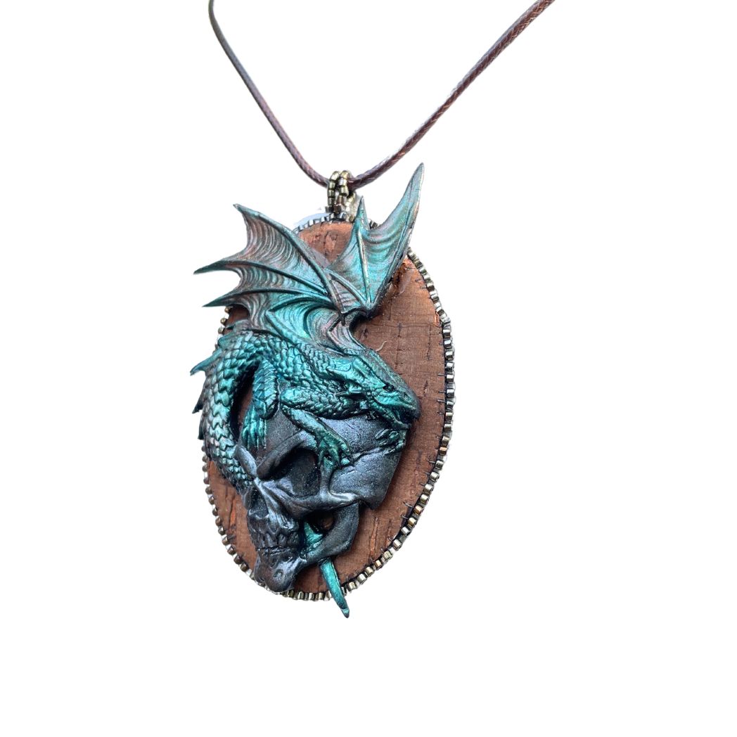 Oval pendant with a polymer clay green dragon upon a silver fierce skull.