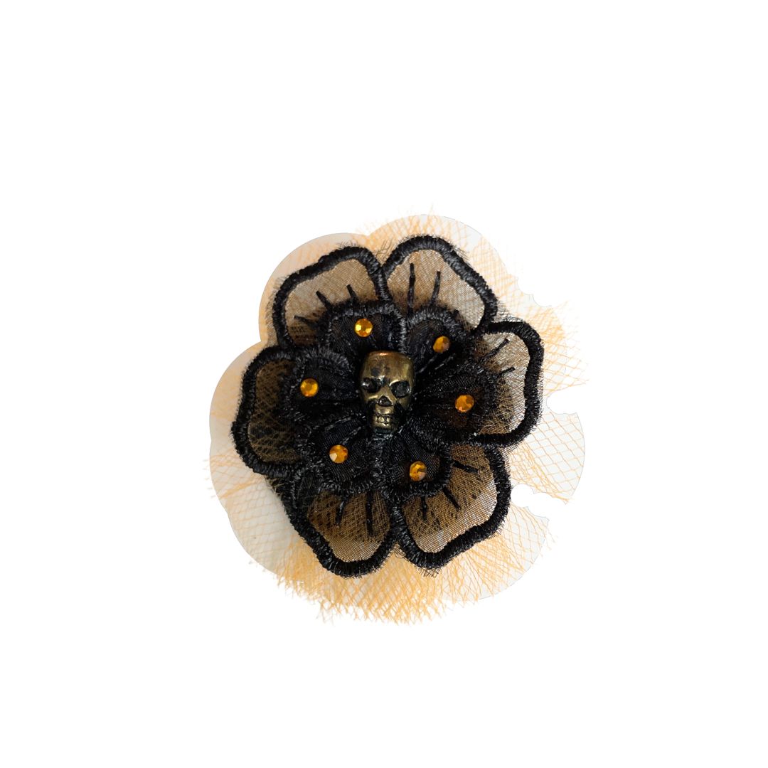 Black flower applique with a gold skull in the center surrounded by orange crystals and orange tulle behind the black flower.