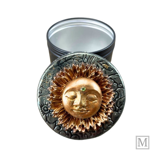 Black storage tin with decorative polymer clay lid with gold sun face design.