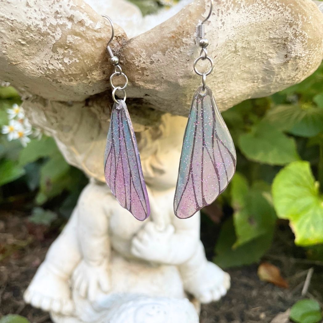 pink and blue wing earrings hanging from a garden ornament.