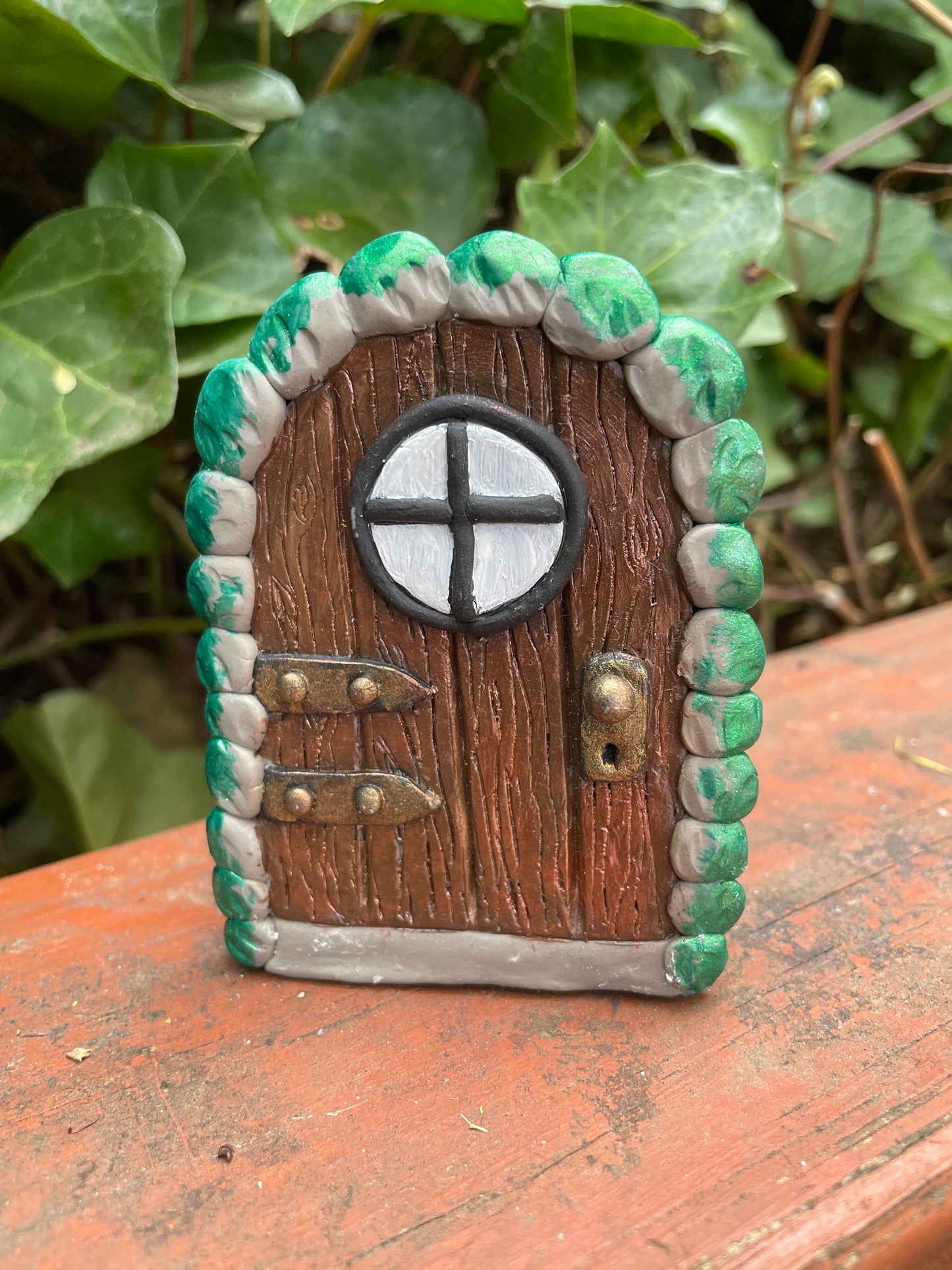 miniture arched elf door ornament against green plants and purple flowers.