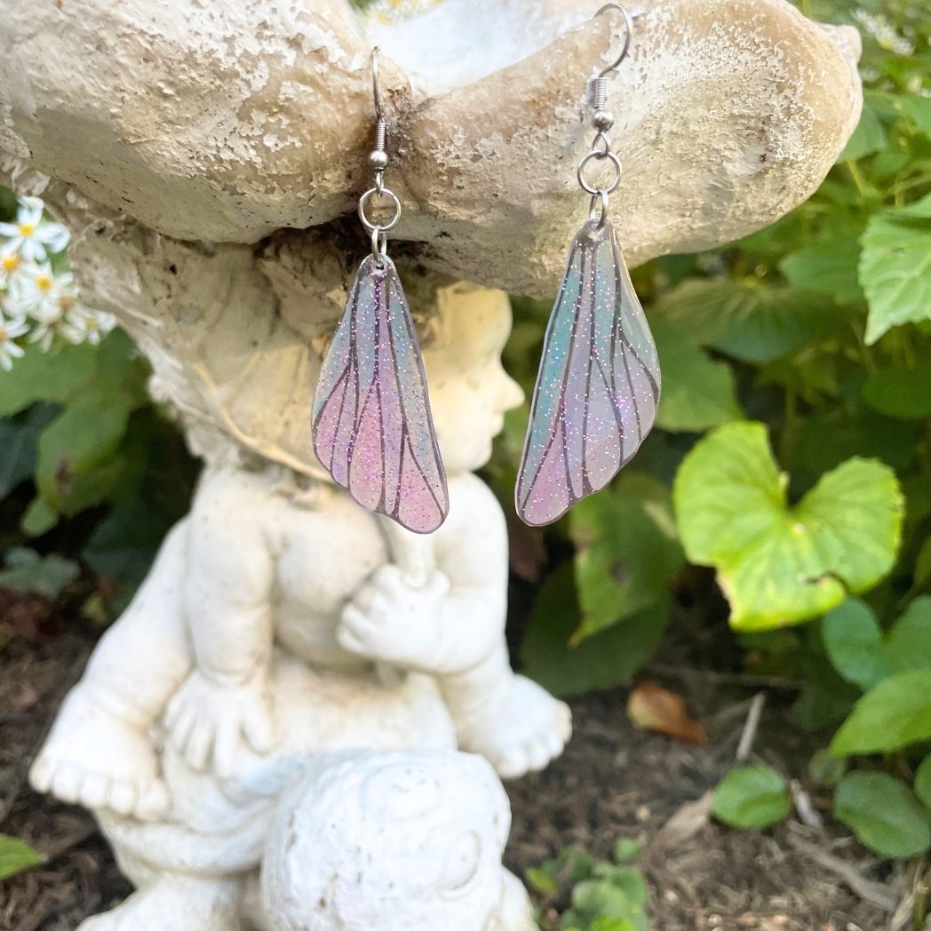 pink and blue wing earrings hanging from a garden ornament.