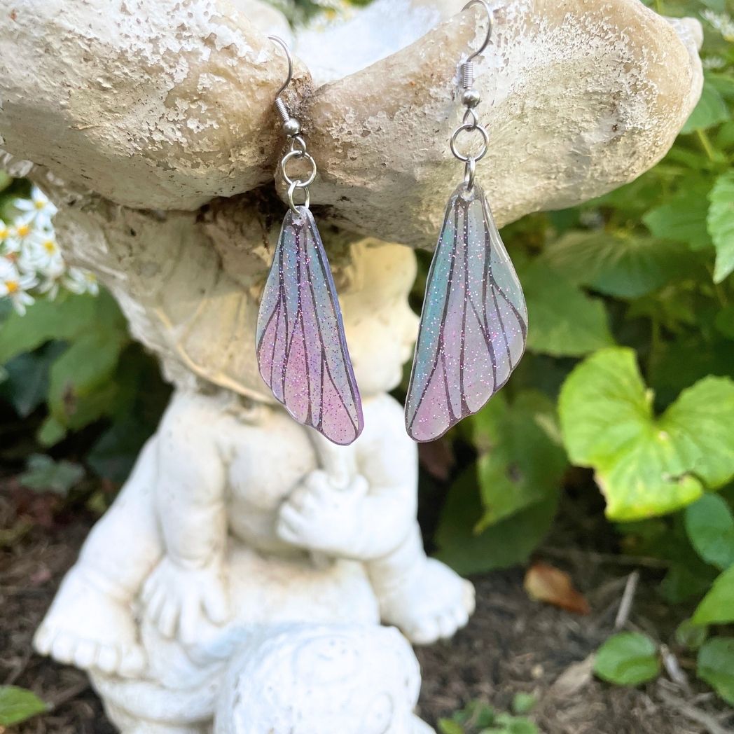 pink and blue wing earrings hanging from a garden ornament.