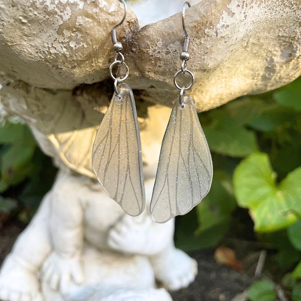 Clear silver glittered wing earring on a garden ornament.