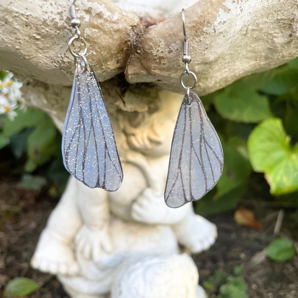 gray small wing earrings hanging on a garden ornment.