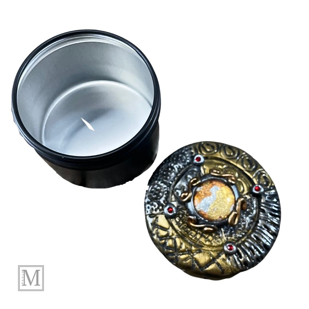 2oz black aluminum storage tin with handcrafted polymer clay lid with foiled glass center orb and gold and silver stamped details and red crystal accents.