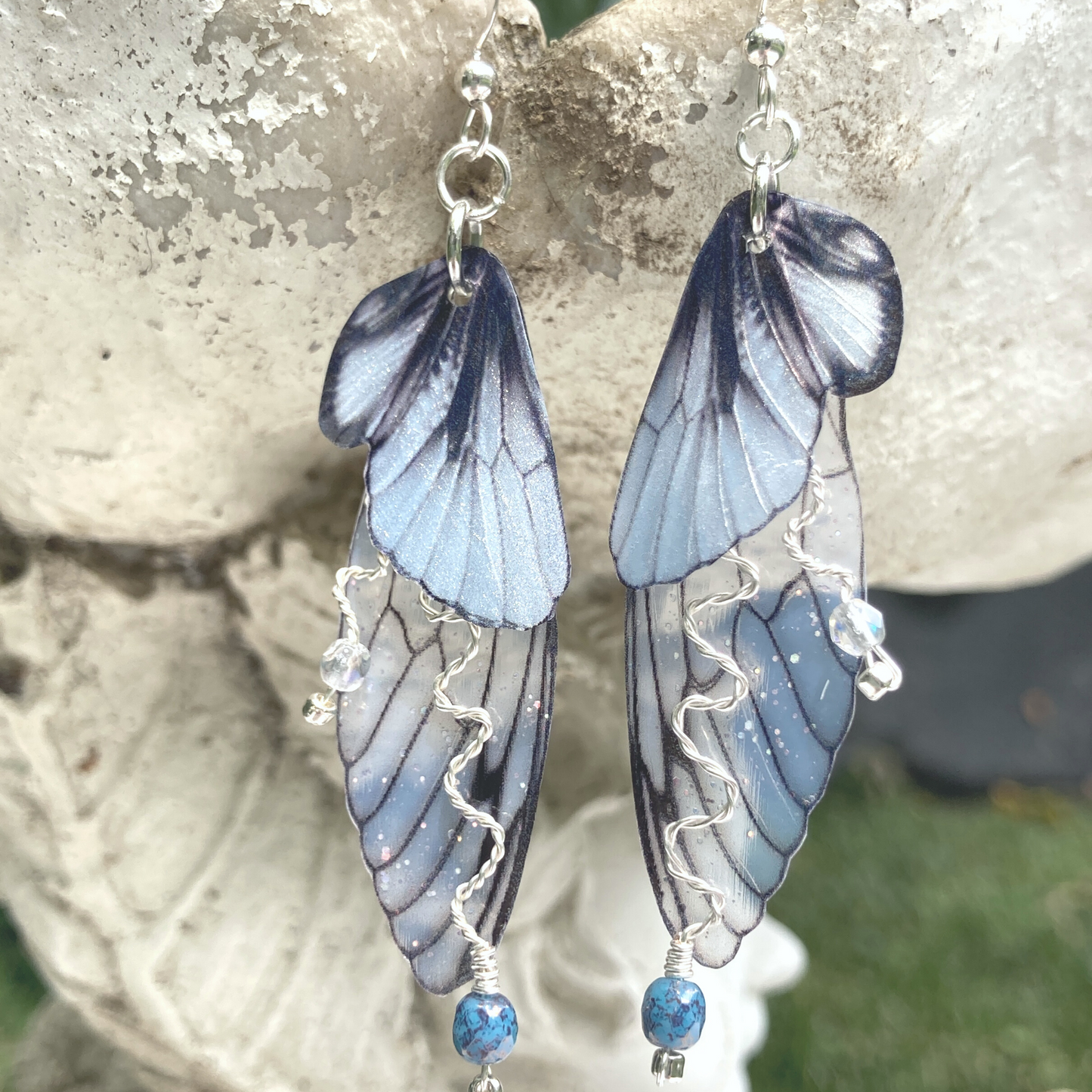 silver double wing fairy earrings with silver twisted wired branches with crystals hanging from a garden ornament