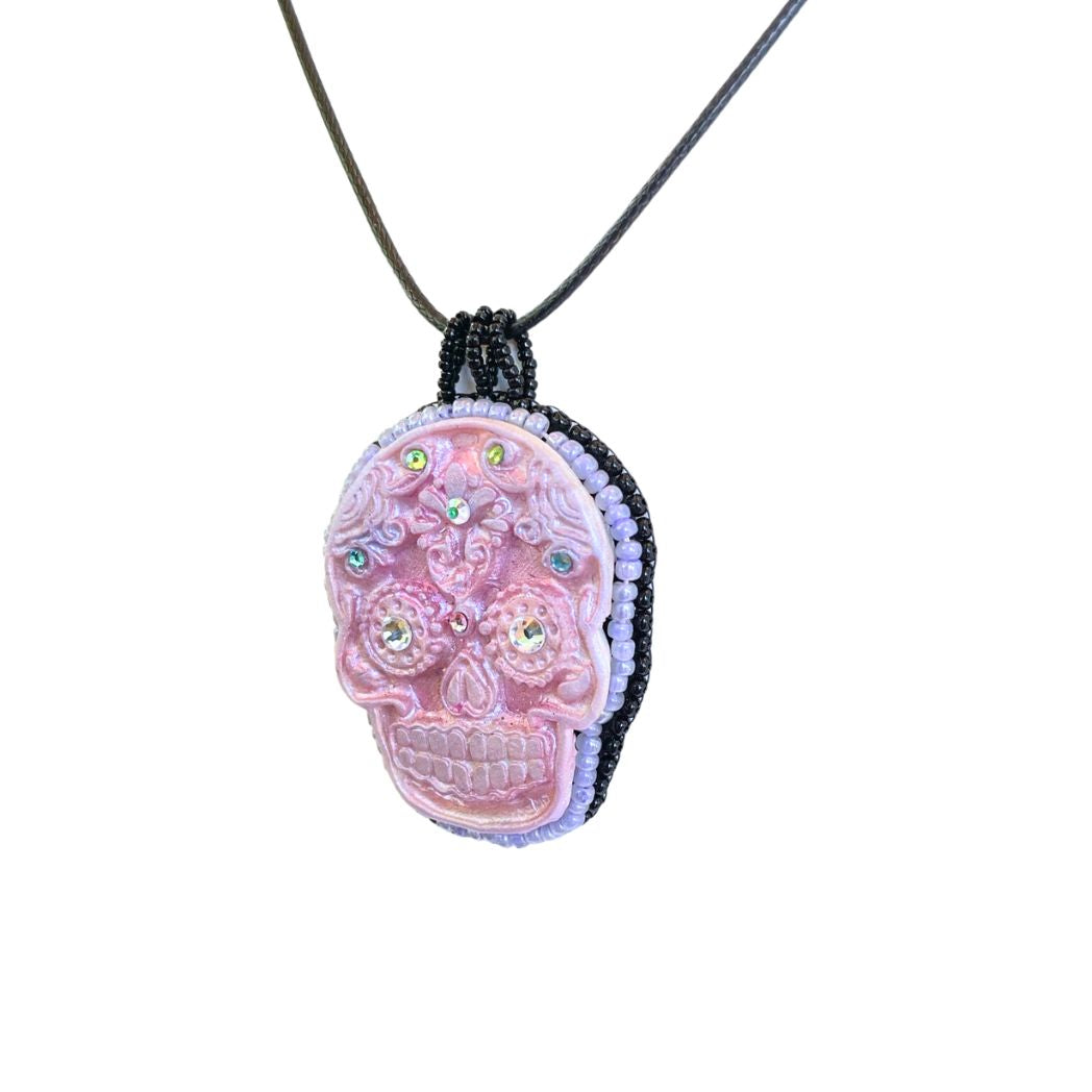 Side view of pink sugar skull necklace with colorful crystal details with seed beaded edging and black cord necklace.