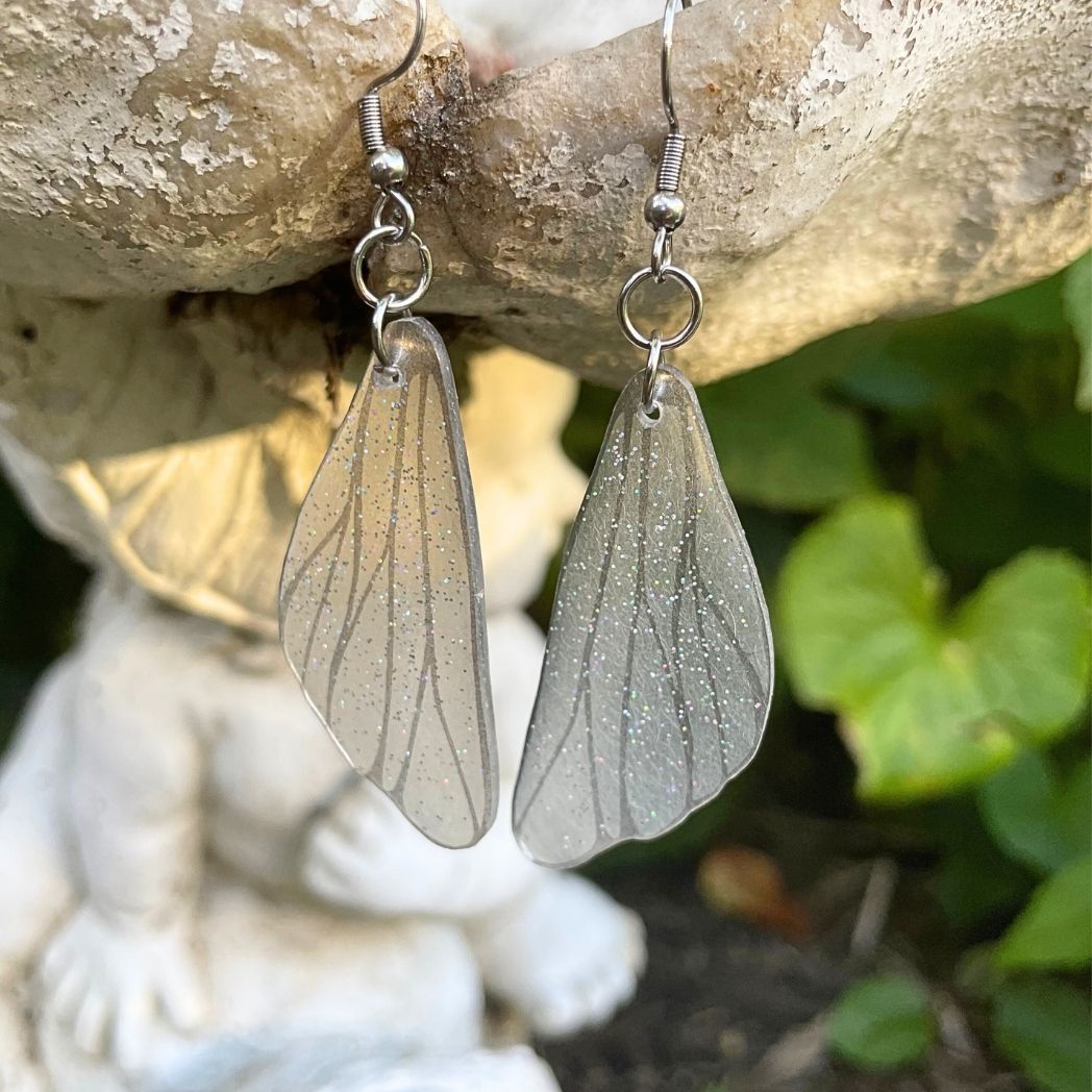 Clear silver glittered wing earring on a garden ornament.