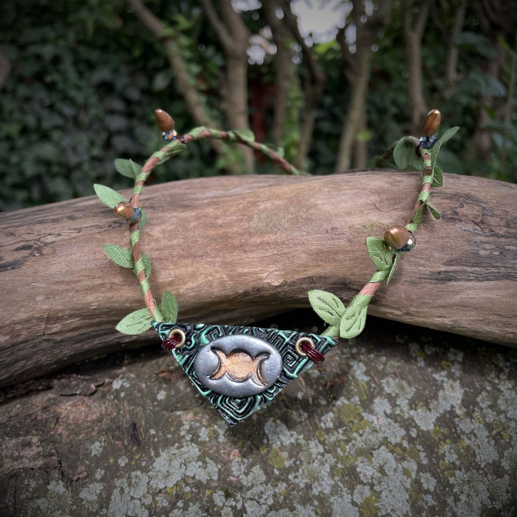 Silver and green triple moon focal on a brown wire and green leaf crown resting on a branch.