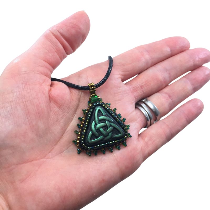 green triquetra symbol pendant held in a hand for size reference against a white background.