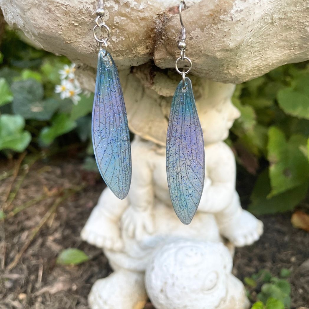 Sparkly glitter turquoise and pink dragonfly wing earrings hanging from a garden ornament.