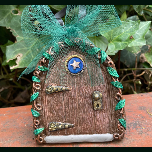 polymer clay small fairy door with a star motif and green tulle bow in a garden setting.