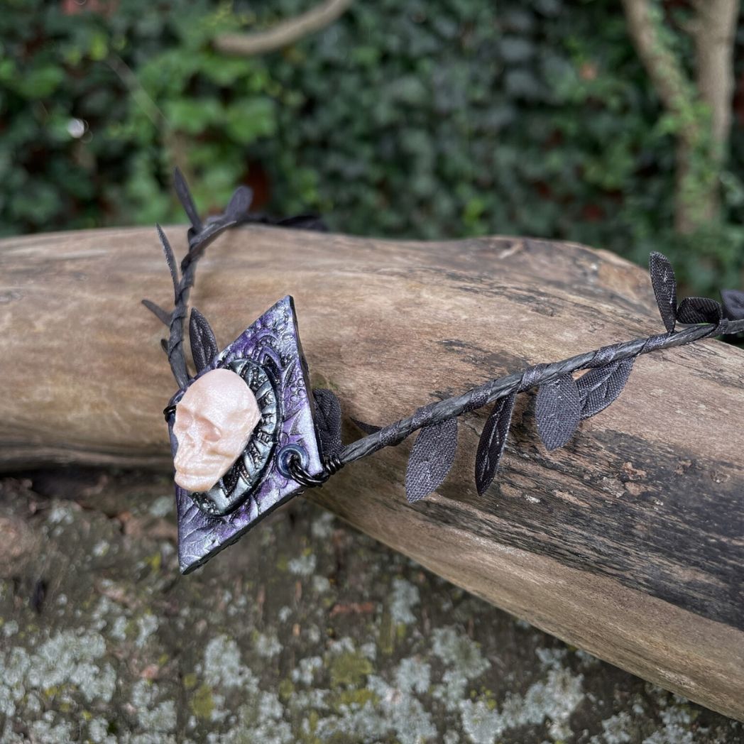 Skull  black leaf wire crown resting on a tree branch.