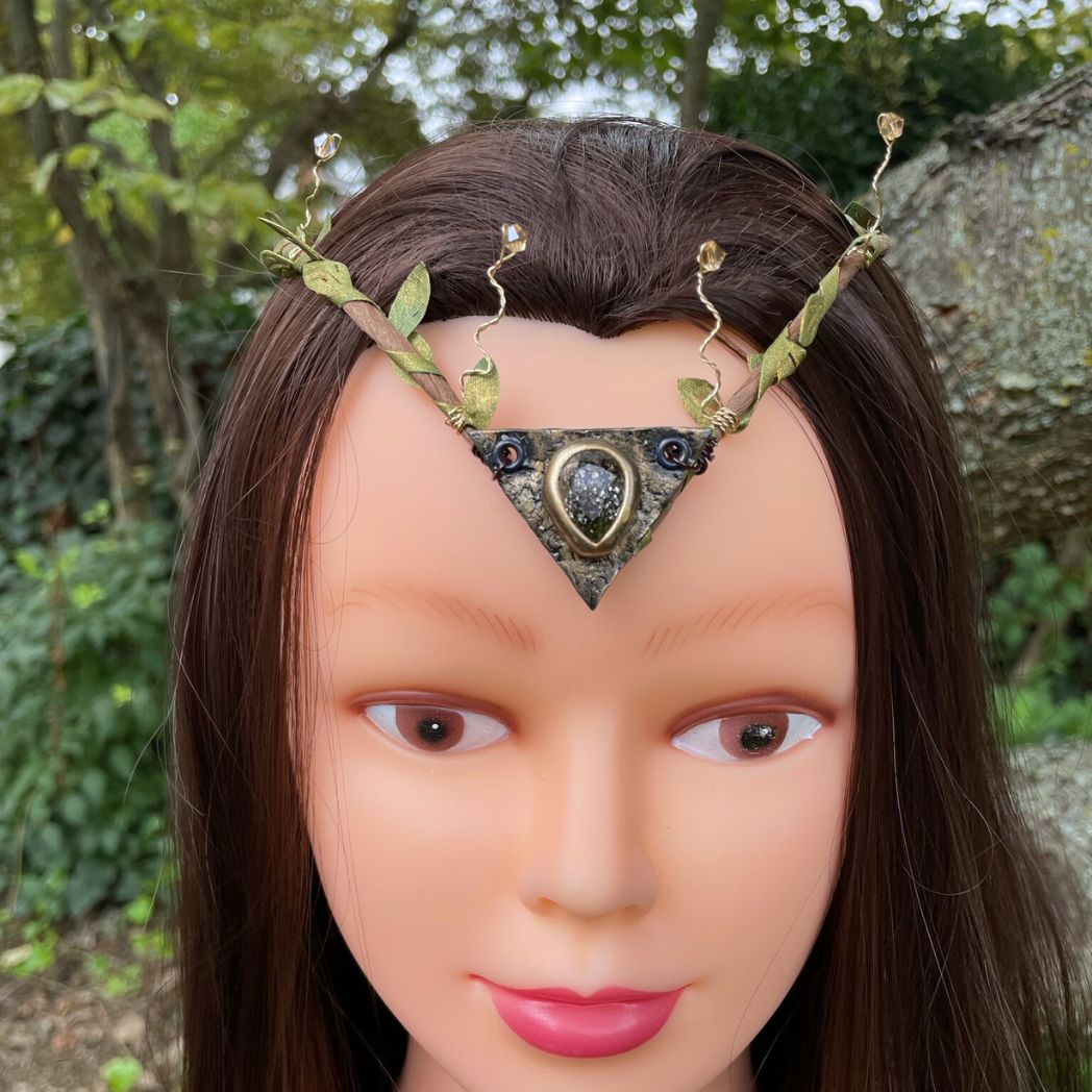 Teadrop crystal focal crwon with brown branches and green fabric leaves. Wired crystals around the sides. Crown sitting on a model.